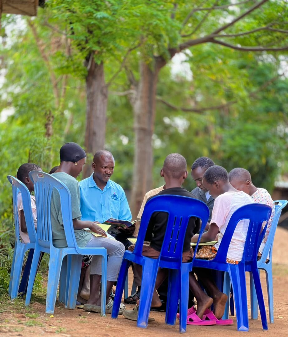 An outdoor Bible study circle seated under the trees